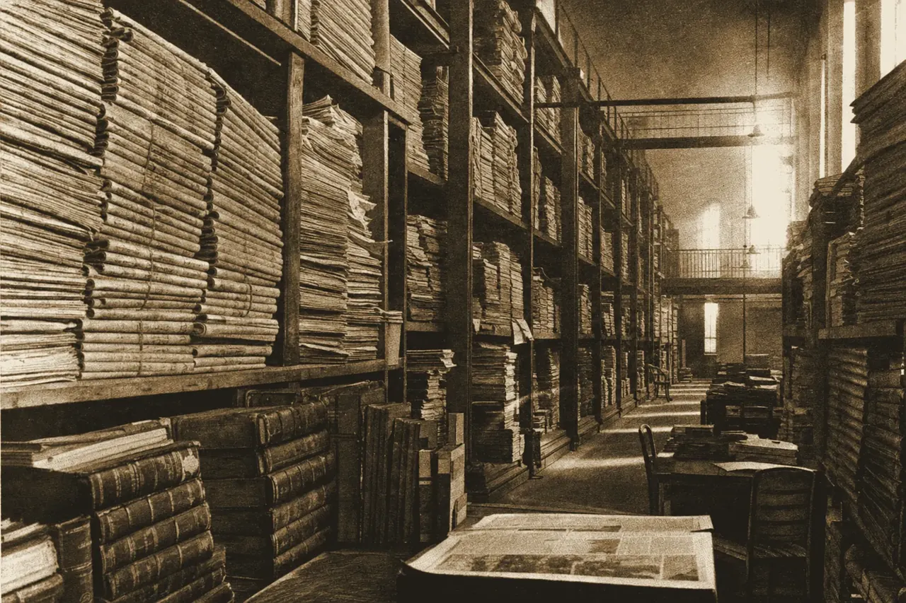 The interior of a vast newspaper archive: towering stacks of bound broadsheet volumes in a dim reading room.